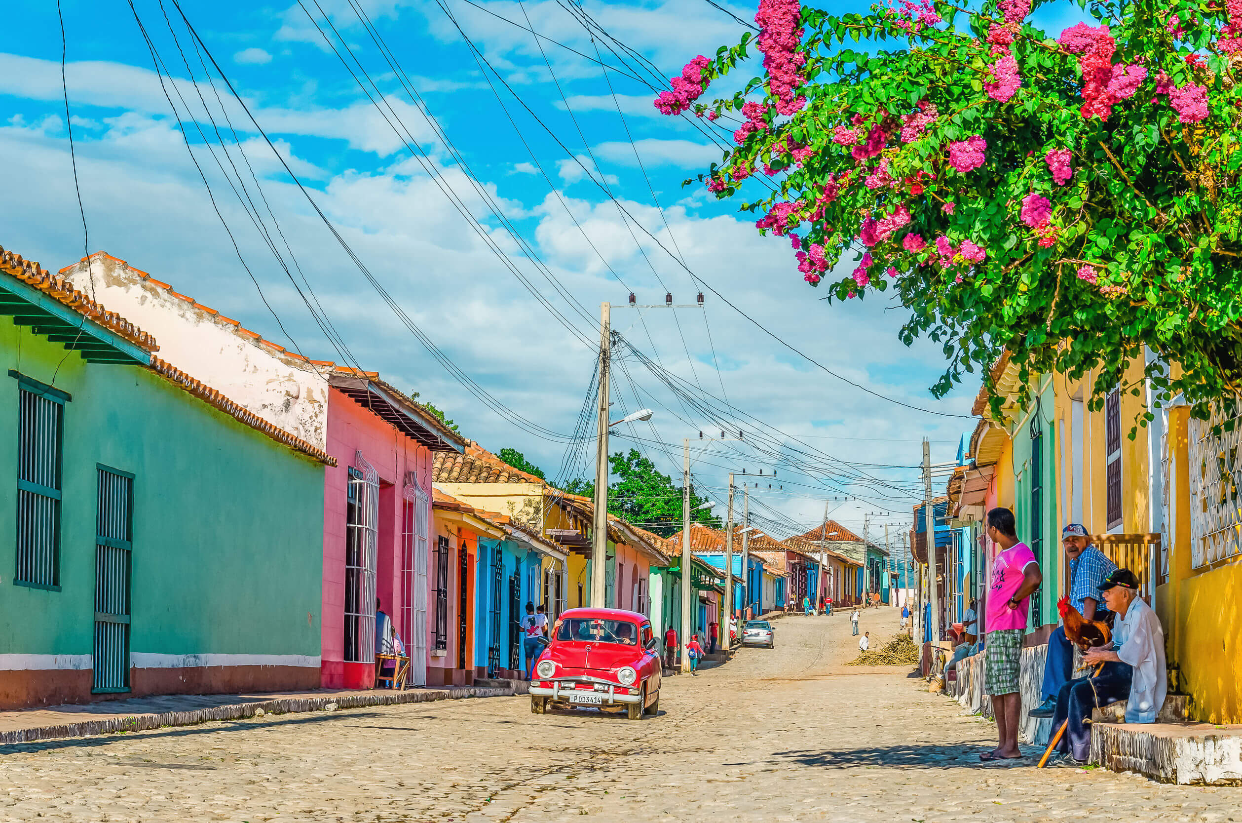 TRINIDAD, CUBA - DECEMBER 8, 2013: Purple and white classic American car and blue colonial building in streets of Trinidad, where old cars are relic of Cuban revolution and still attracts tourists.