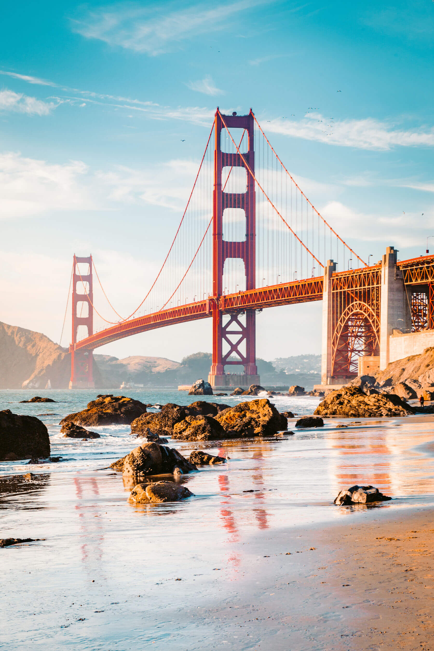 Classic panoramic view of famous Golden Gate Bridge seen from scenic Baker Beach in beautiful golden evening light on a sunny day with blue sky and clouds in summer, San Francisco, California, USA