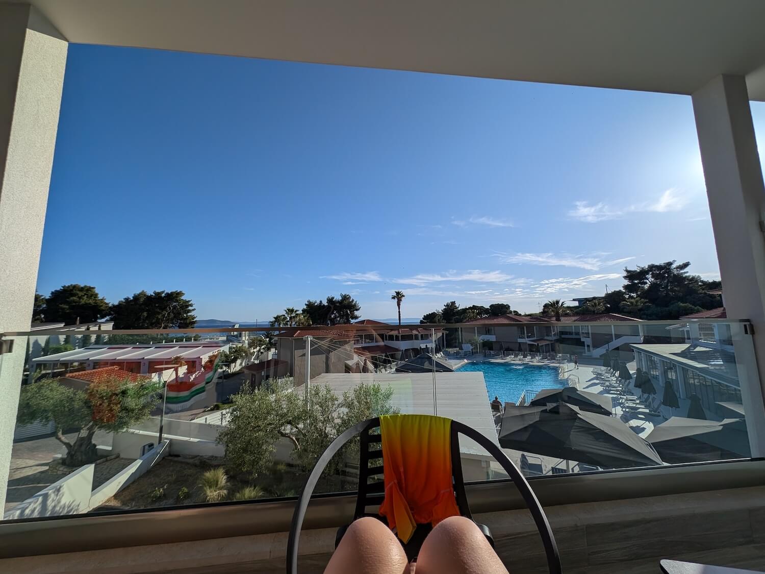 a person's legs in a chair by a window overlooking a pool