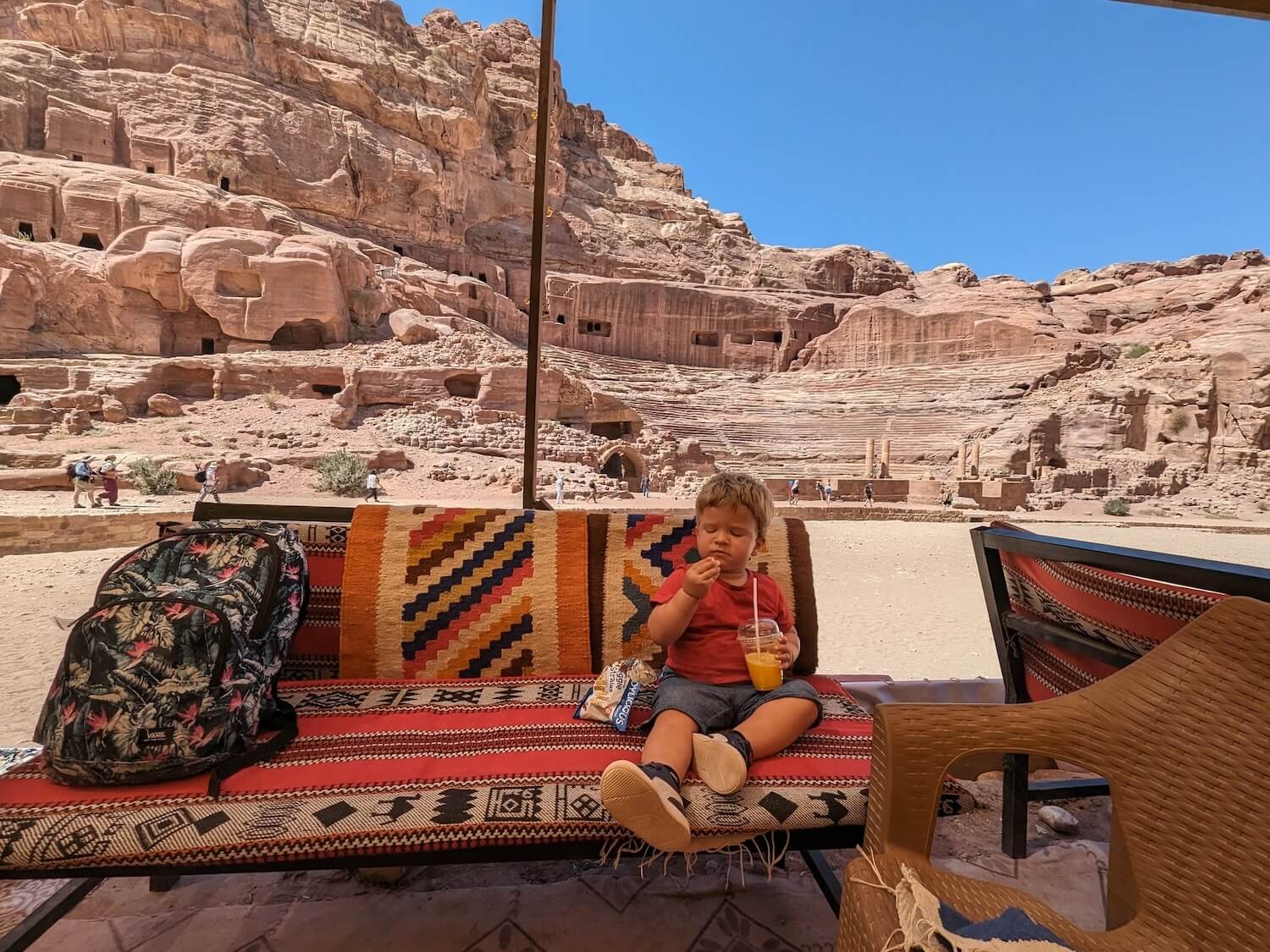 a child sitting on a bench outside with a red and yellow drink