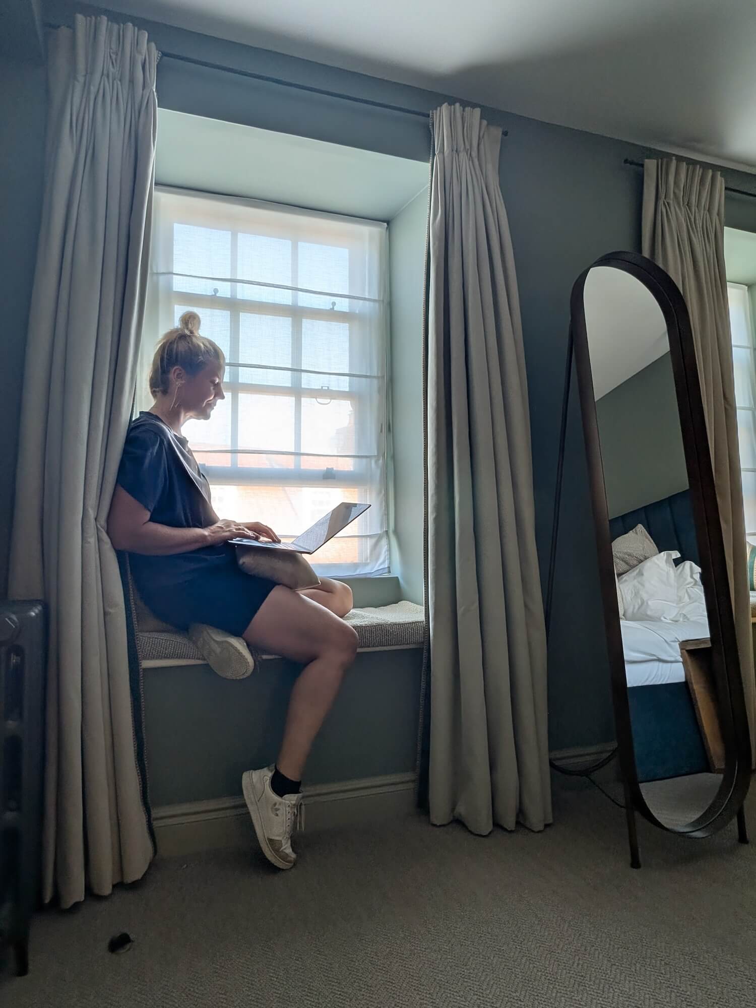 a woman sitting on a window sill with a laptop