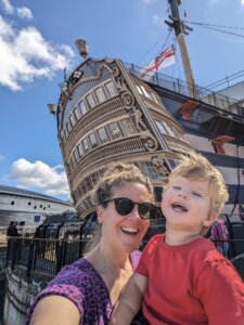 a woman and child taking a selfie in front of a tall ship