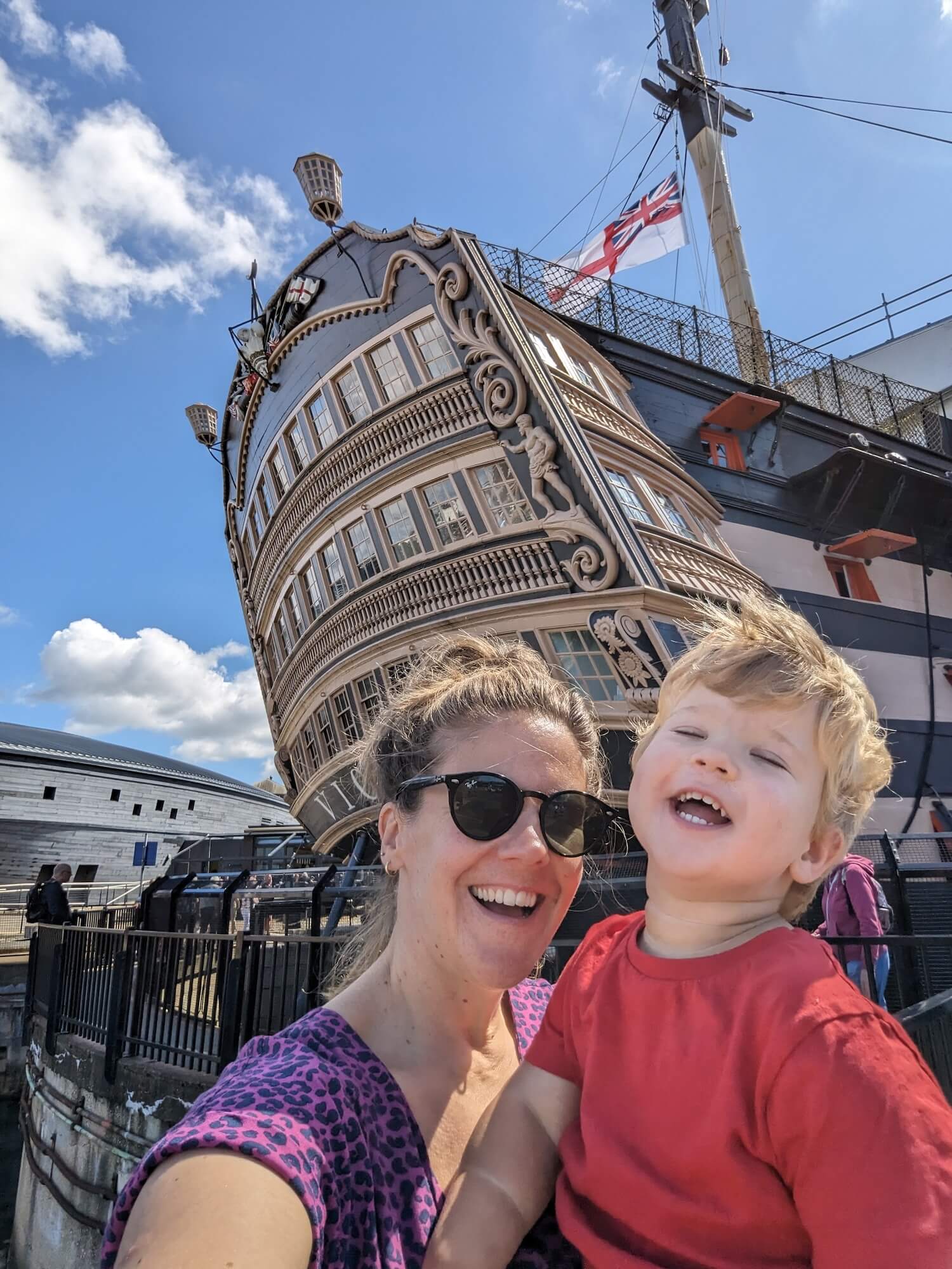 a woman and child taking a selfie in front of a tall ship